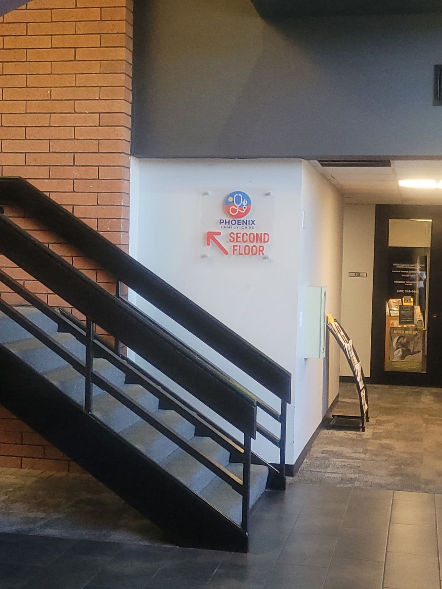 Interior stairwell with a Phoenix Family Care sign and a red arrow pointing up to the second floor